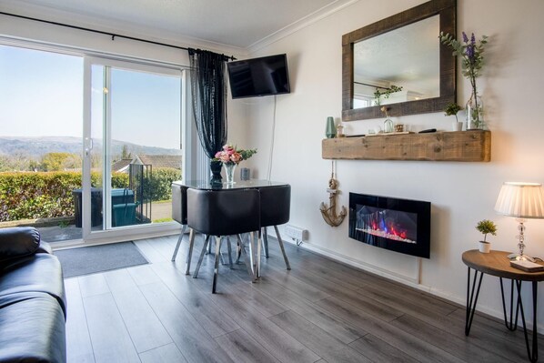 Una sala de estar moderna con un sofá, televisor, chimenea y vistas al exterior.