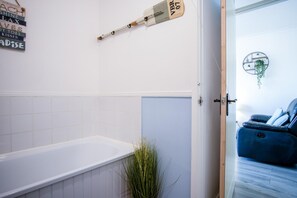 Un baño con una bañera blanca, un perchero con toalla y una planta en maceta.