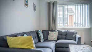 Ein Wohnzimmer mit grauem Sofa, einem gelben Kissen und einem Couchtisch mit Holzbeschichtung und Metallelementen.