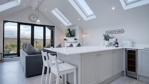 A modern kitchen with a large island, a dining area with a sofa and chairs, and a view of the countryside through large windows.