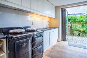 A modern kitchen with white cabinets, a black stove, and a sink. - Bwthyn Berwig - 3 Bedroom Cottage - Llanrhidian (Swansea)