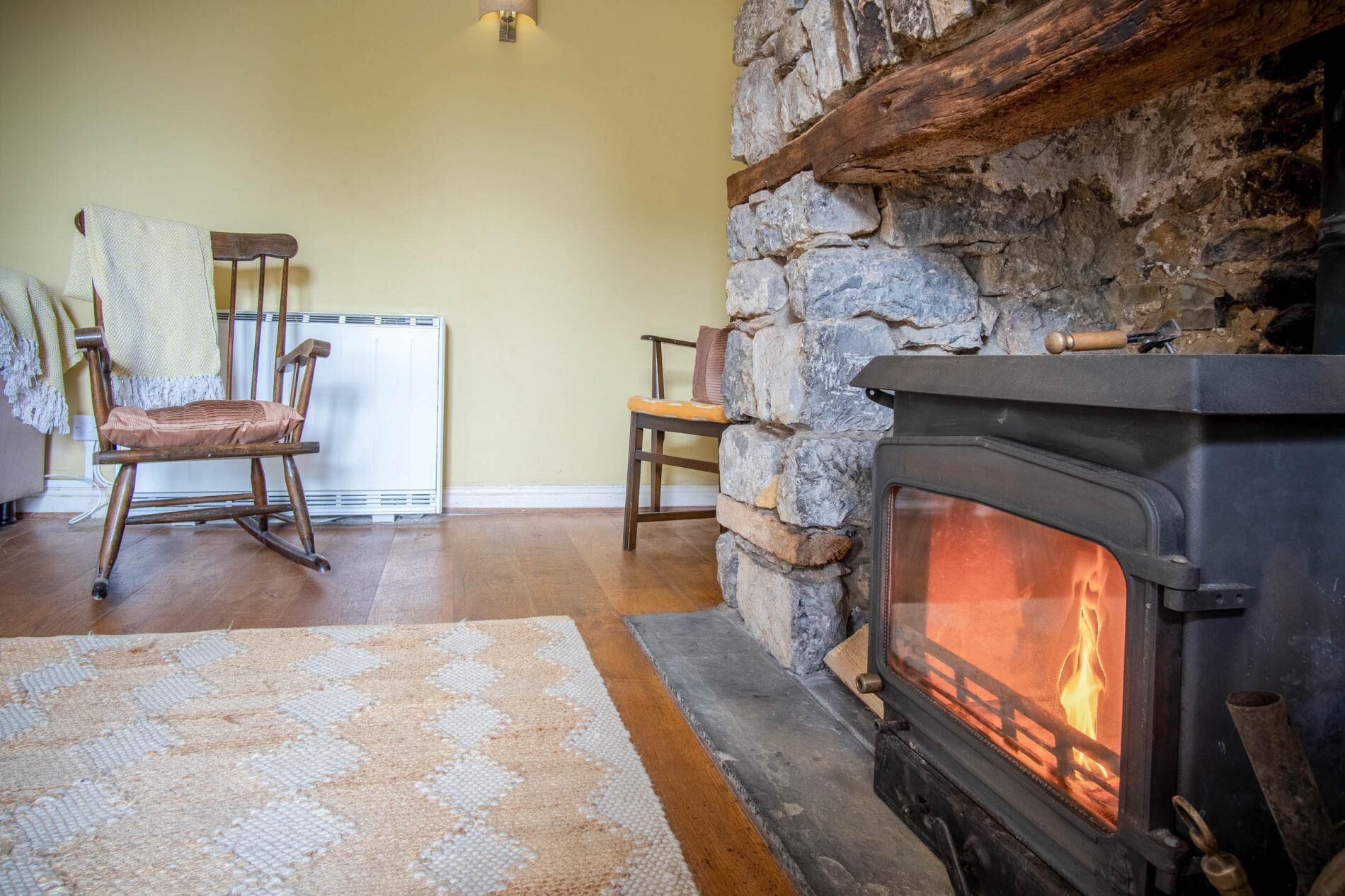 Un salon chaleureux avec une cheminée en pierre, un fauteuil à bascule en bois et un radiateur.