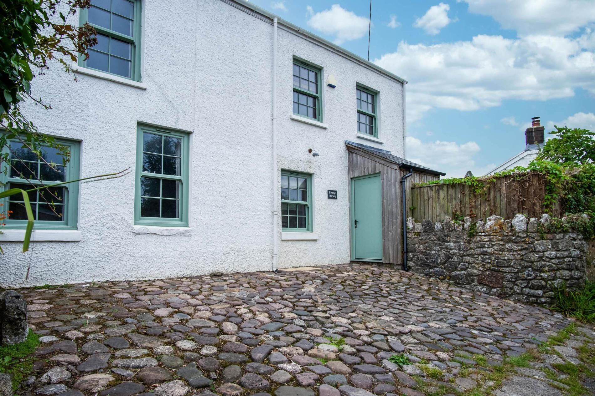 A white building with green windows and a stone wall.