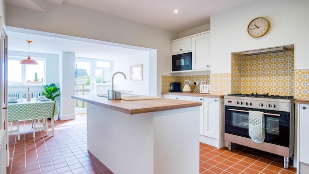 A kitchen with a central island, white cabinets, a microwave, a stove, and a clock on the wall.