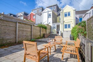 A courtyard with wooden furniture and a brick wall. - Woodville Road - 2 Bedroom House - Mumbles (Swansea)