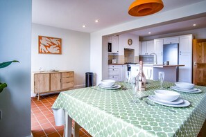 A dining area with a green patterned tablecloth, white plates, and a bottle of champagne. There is a wooden cabinet and a trash bin in the background. - Woodville Road - 2 Bedroom House - Mumbles (Swansea)