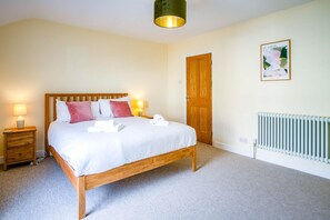A bedroom with a wooden bed, bedside lamps, a radiator, and a door. - Woodville Road - 2 Bedroom House - Mumbles (Swansea)