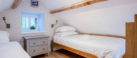 A bedroom with a wooden bed, a nightstand, a window with blinds, and a wall-mounted lamp.
