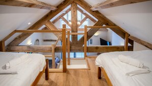 A high-ceilinged attic bedroom with wooden beams, two beds, and a skylight.