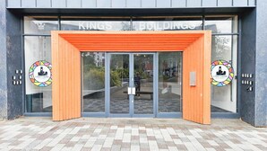 L’entrée d’un bâtiment à l’architecture moderne, caractérisée par une grande porte vitrée et un arc en bois.