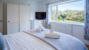 Un dormitorio con cama, televisor y ventana con vista a la vegetación.