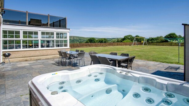 Un jardin avec un jacuzzi, du mobilier d’extérieur, un barbecue et un patio fermé par des baies vitrées.