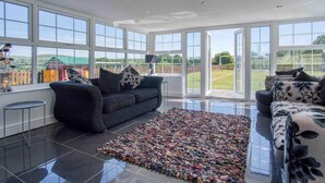 Un salon spacieux avec de grandes fenêtres, un canapé gris foncé, un tapis à motifs et une vue sur l’extérieur.
