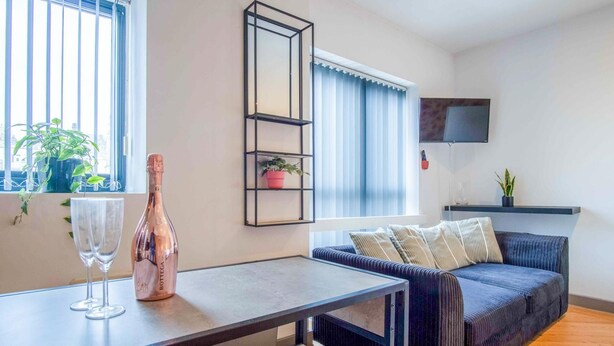 Ein modernes Wohnzimmer mit einer Couch, einem Couchtisch, einem an der Wand befestigten Fernseher und einem Fenster mit Jalousien.