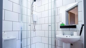 Ein modernes Badezimmer mit weißen Fliesen, einer Duschkabine aus Glas, einem weißen Waschbecken und einem Spiegel darüber.