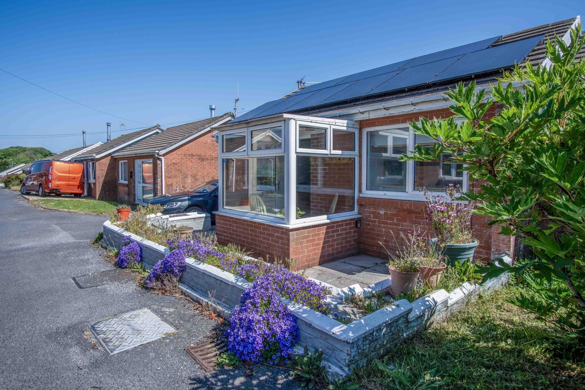 A residential house with a conservatory, brick exterior, and a garden with purple flowers.