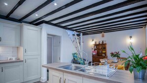Une cuisine moderne avec des meubles blancs, un évier en acier inoxydable et un escalier en bois menant à un coin repas.
