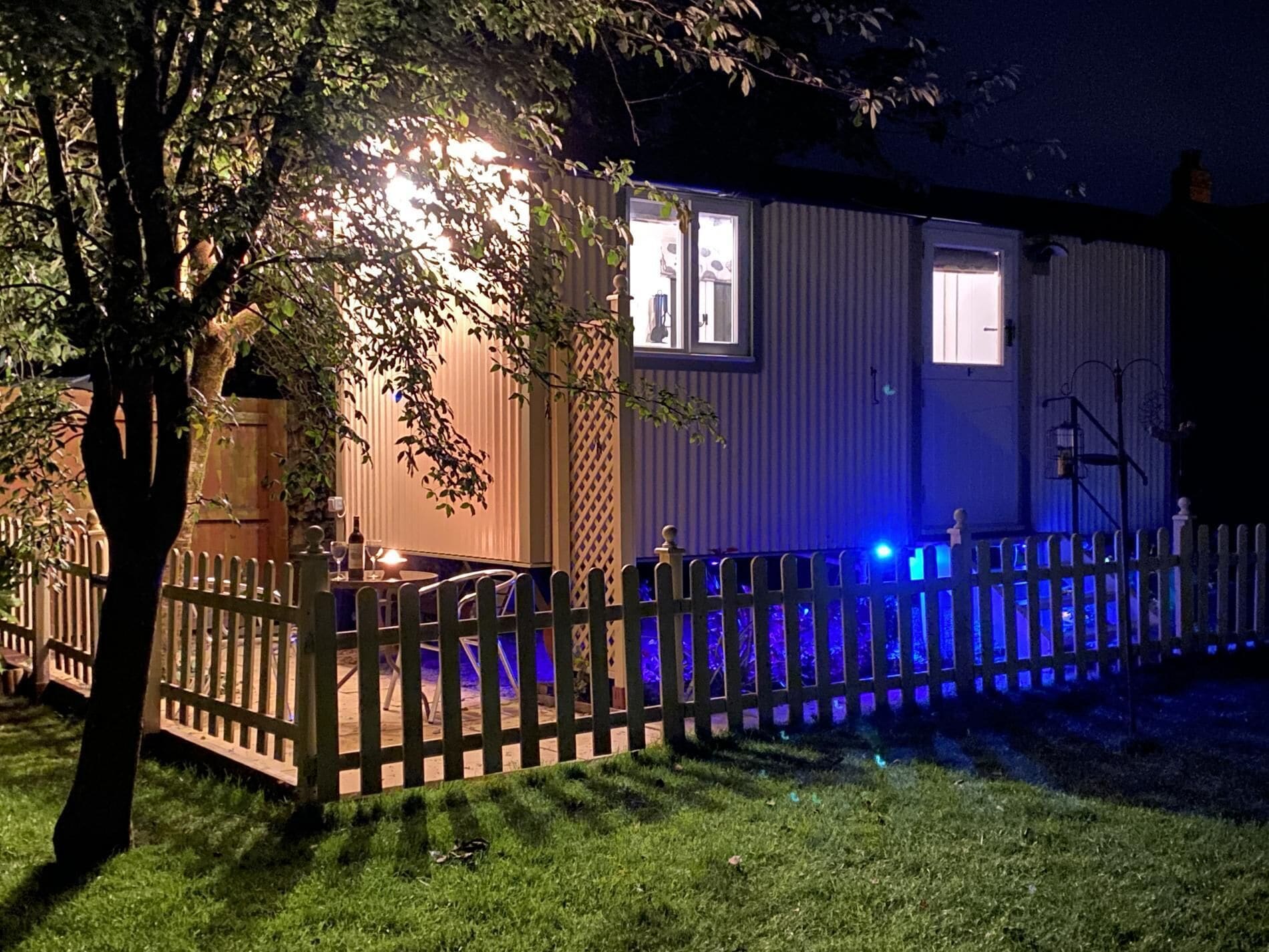 A house with a fenced yard, a tree, and a lit window.