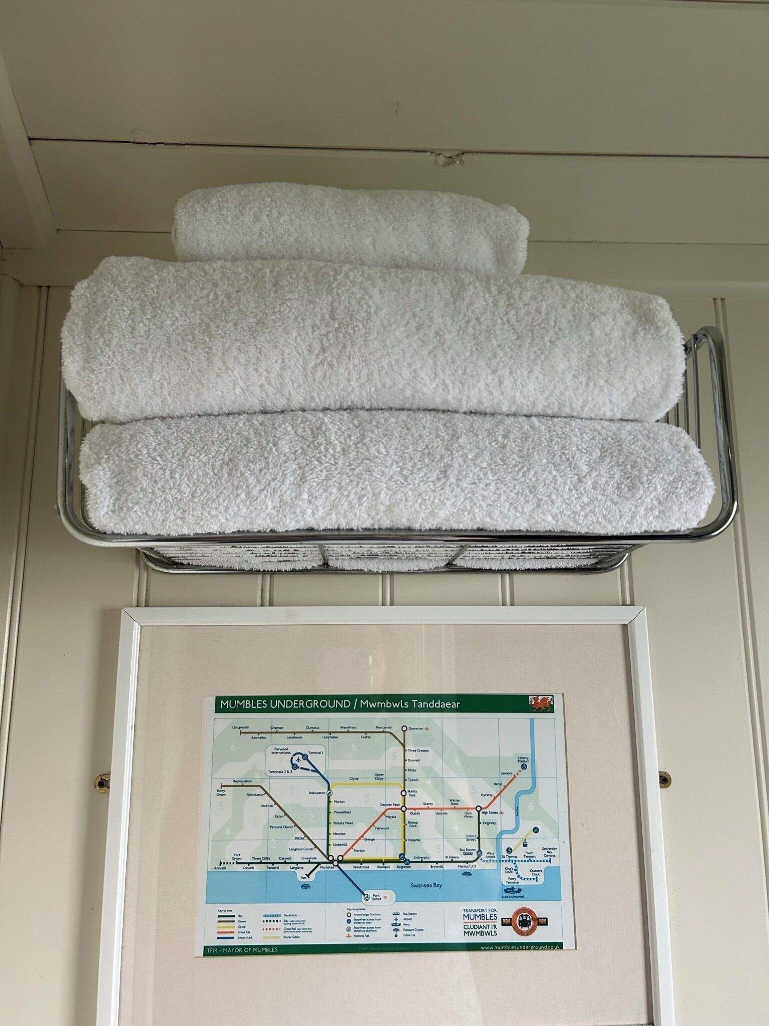 A framed map of the Mumbles Underground with a metal towel rack above it.