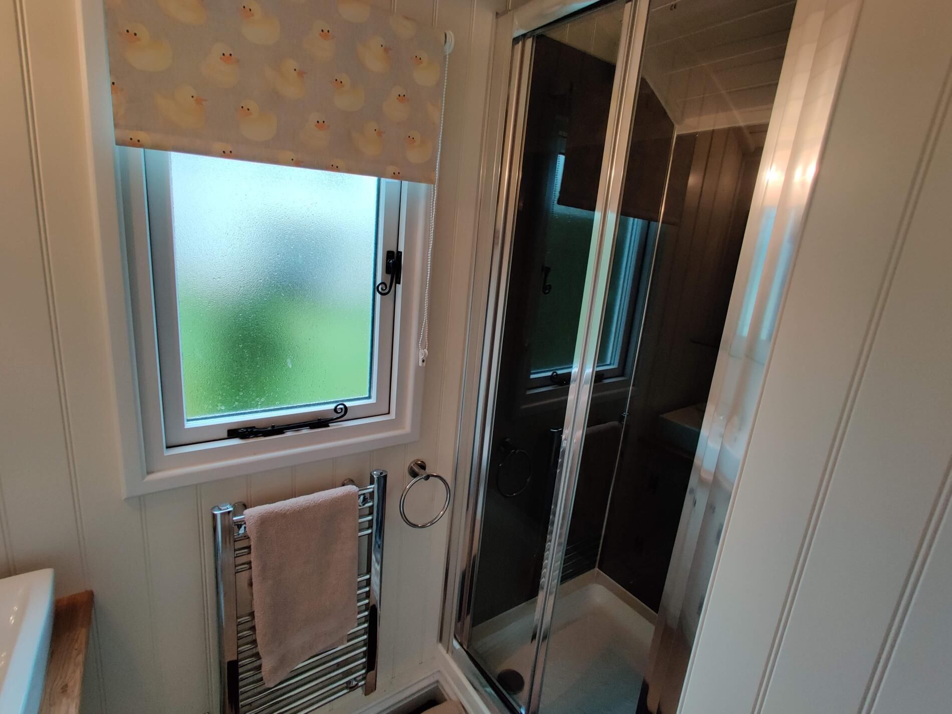 A bathroom with a frosted glass window, a towel rack, and a shower enclosure.