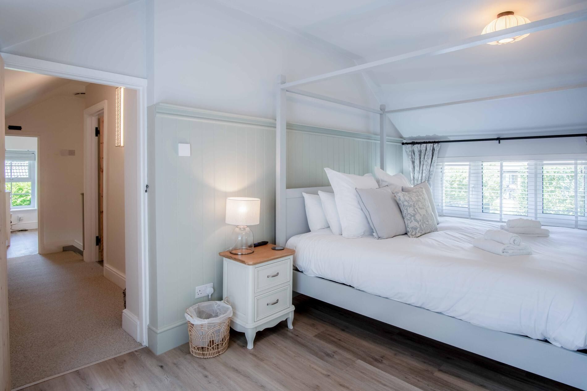 Een slaapkamer met een bed, nachtkastje, lamp en uitzicht op het natuurlijke landschap door het raam.
