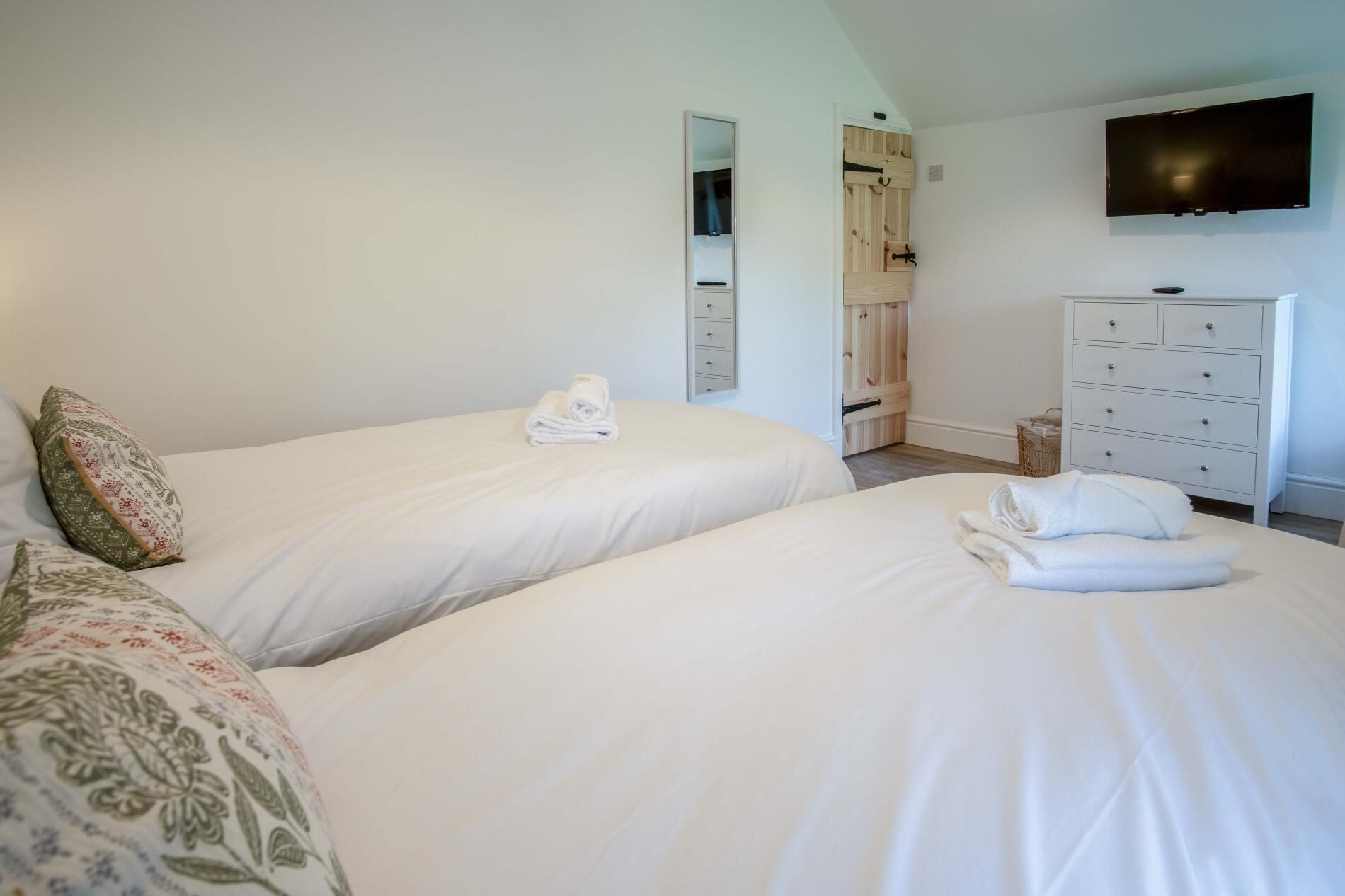 A hotel room with two beds, a TV mounted on the wall, and a wooden wardrobe.