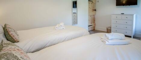 A hotel room with two beds, a TV mounted on the wall, and a wooden wardrobe.