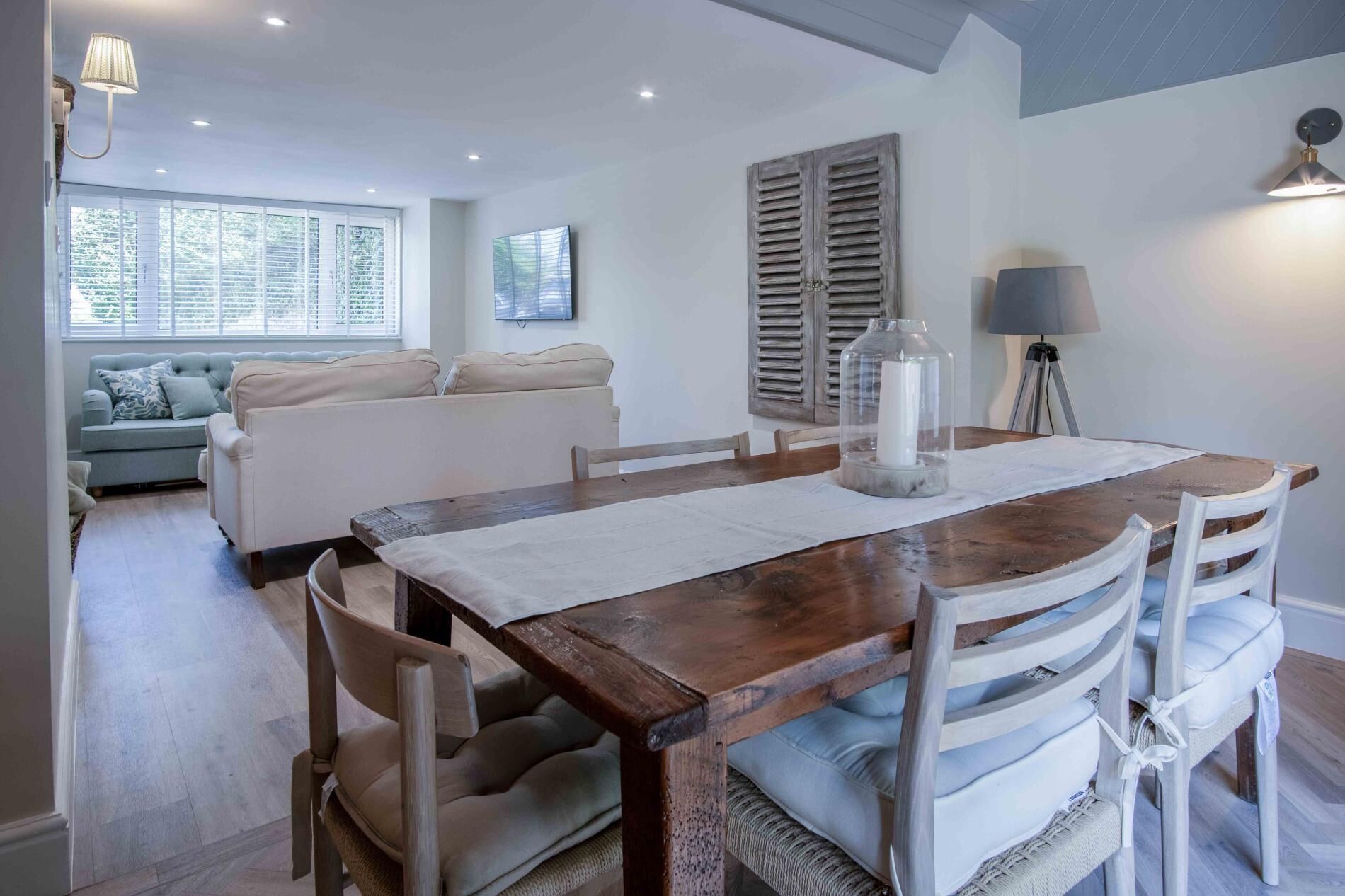 Un coin repas avec une table en bois, des chaises à revêtement blanc et un porte-bougie en verre.