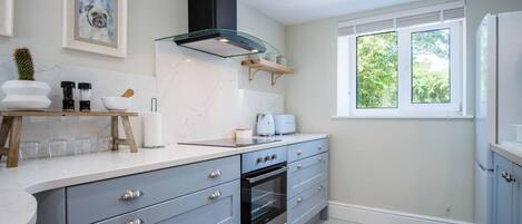 A modern kitchen with grey cabinets, a built-in oven, a black range hood, and a window with a view of greenery.