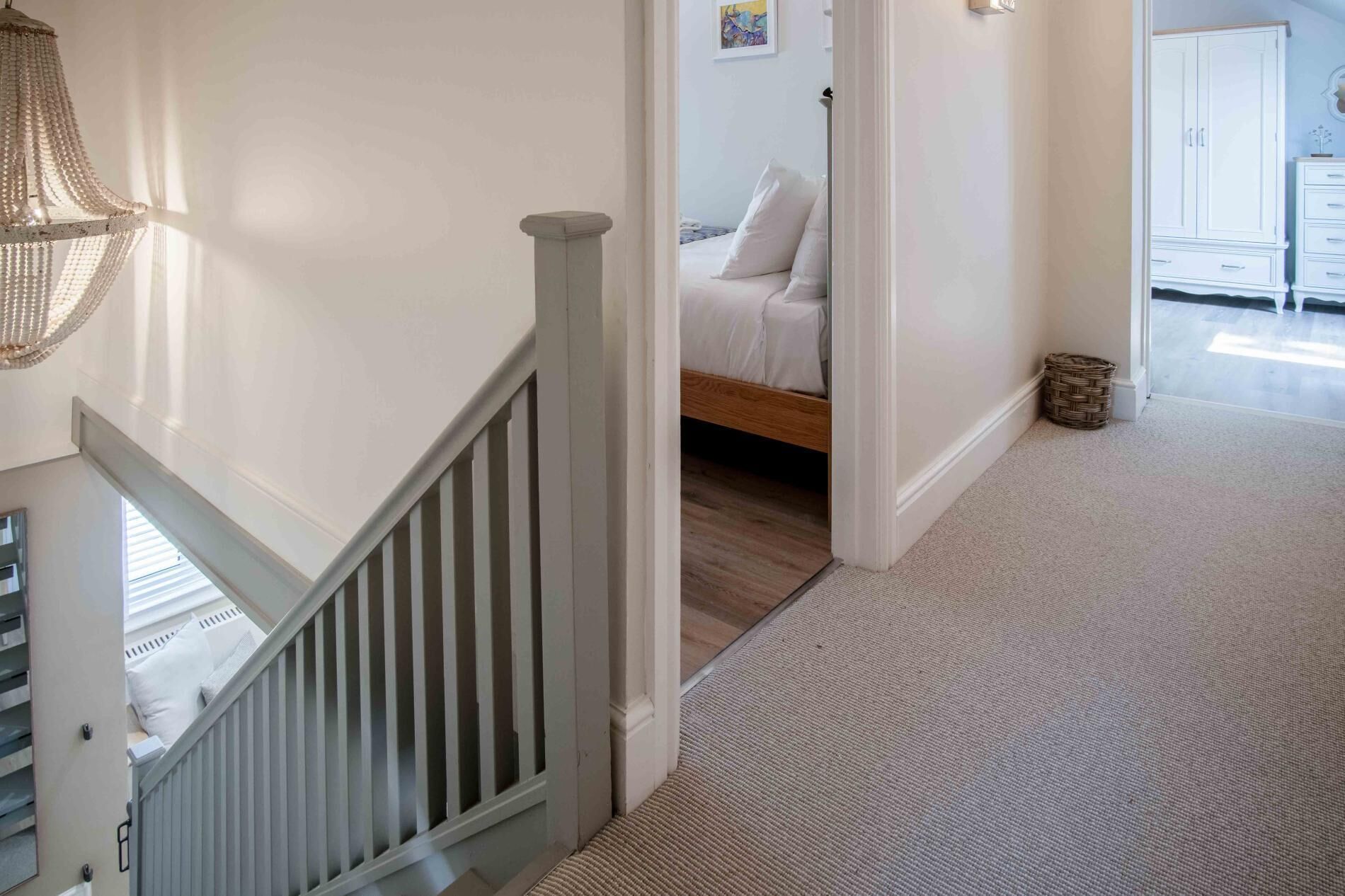 A staircase with a white railing leading to a bedroom with a wooden floor and a bed with white bedding.