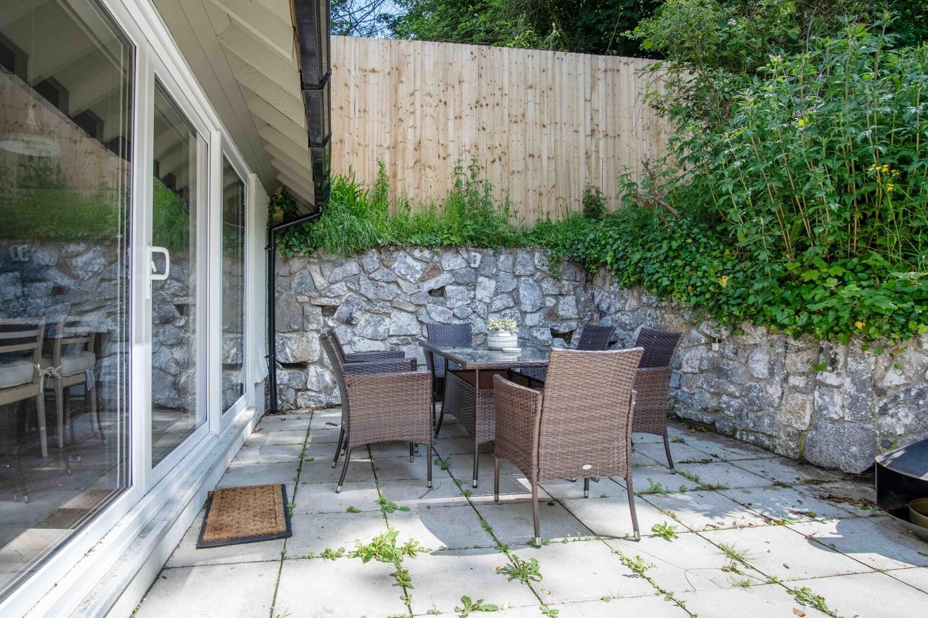 Eine Terrasse mit Korbmöbeln, einer Steinmauer und einem Holzzaun.
