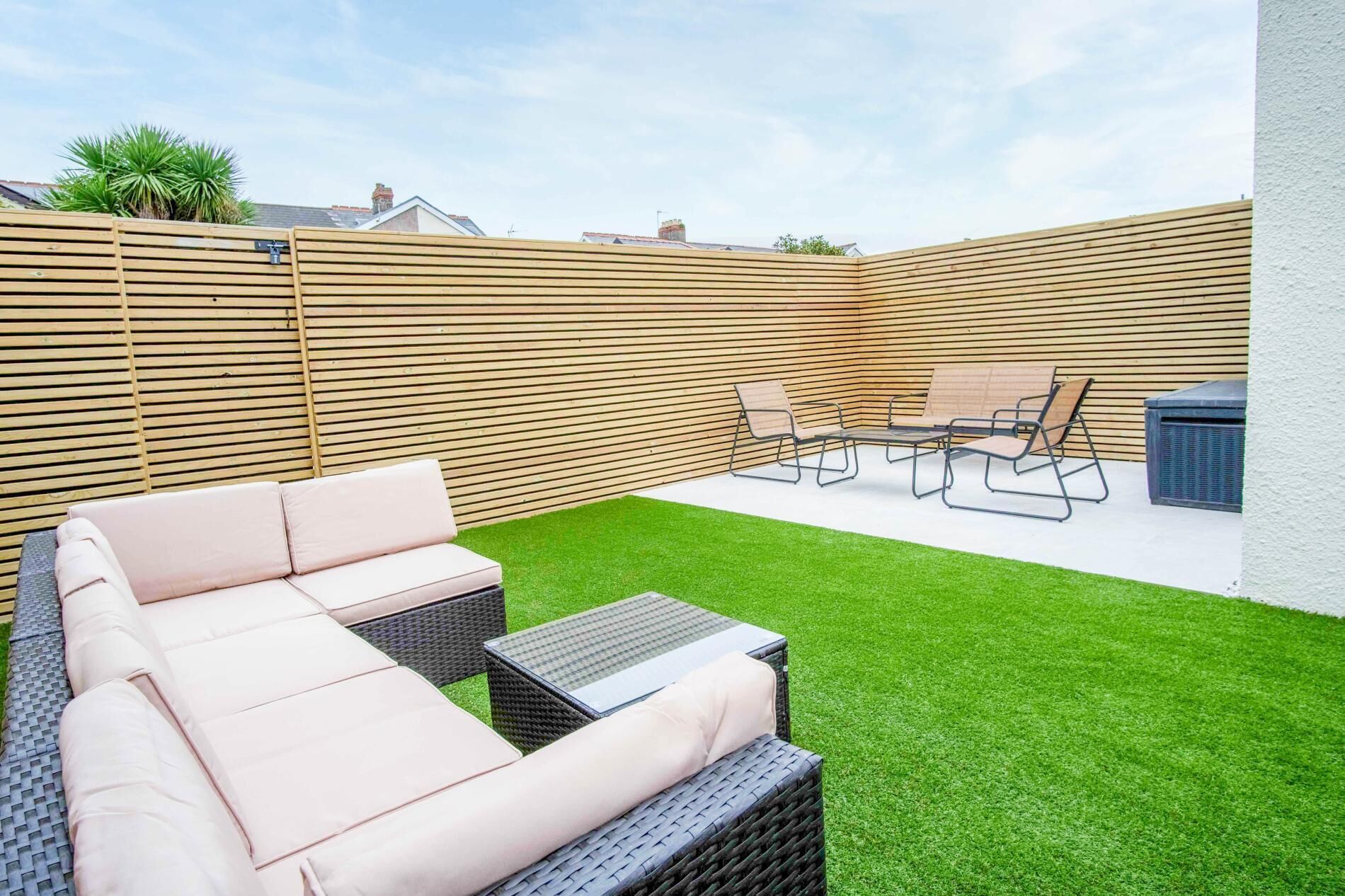 Un jardin avec une pelouse verdoyante, une clôture en bois et du mobilier d’extérieur comprenant un canapé et des fauteuils.