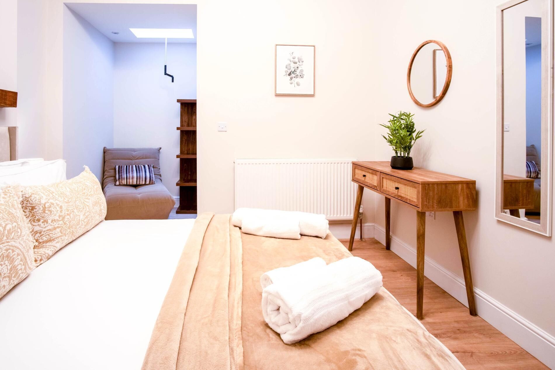 Een slaapkamer met een bed, een nachtkastje met een plant, een spiegel en een radiator.