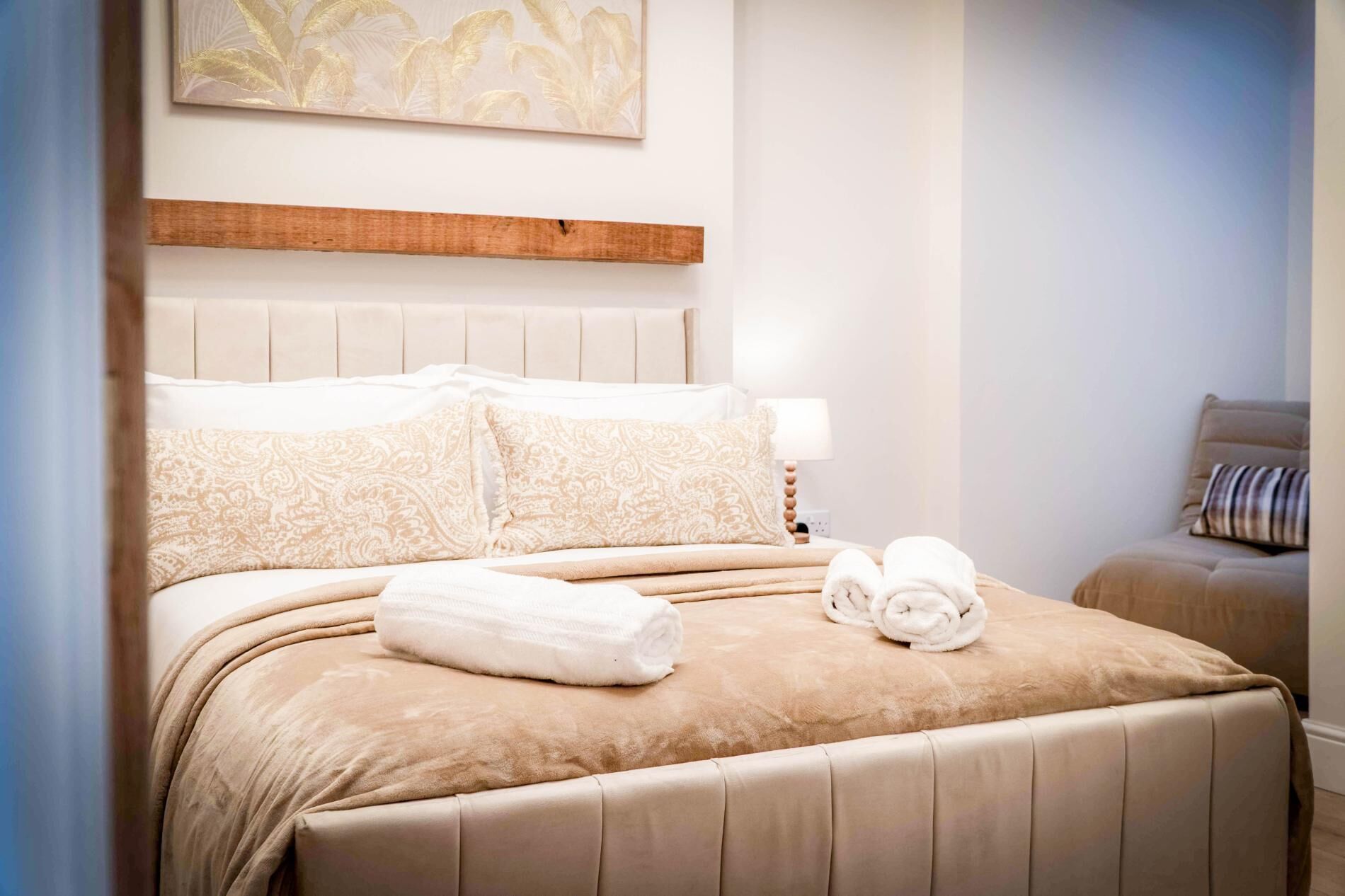A hotel room with a bed, a headboard, a bedside table, a lamp, and a wall-mounted artwork.
