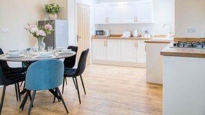 Une cuisine moderne avec des meubles blancs, un coin repas doté d’une table ronde et de chaises, et un petit îlot central avec une plaque de cuisson.