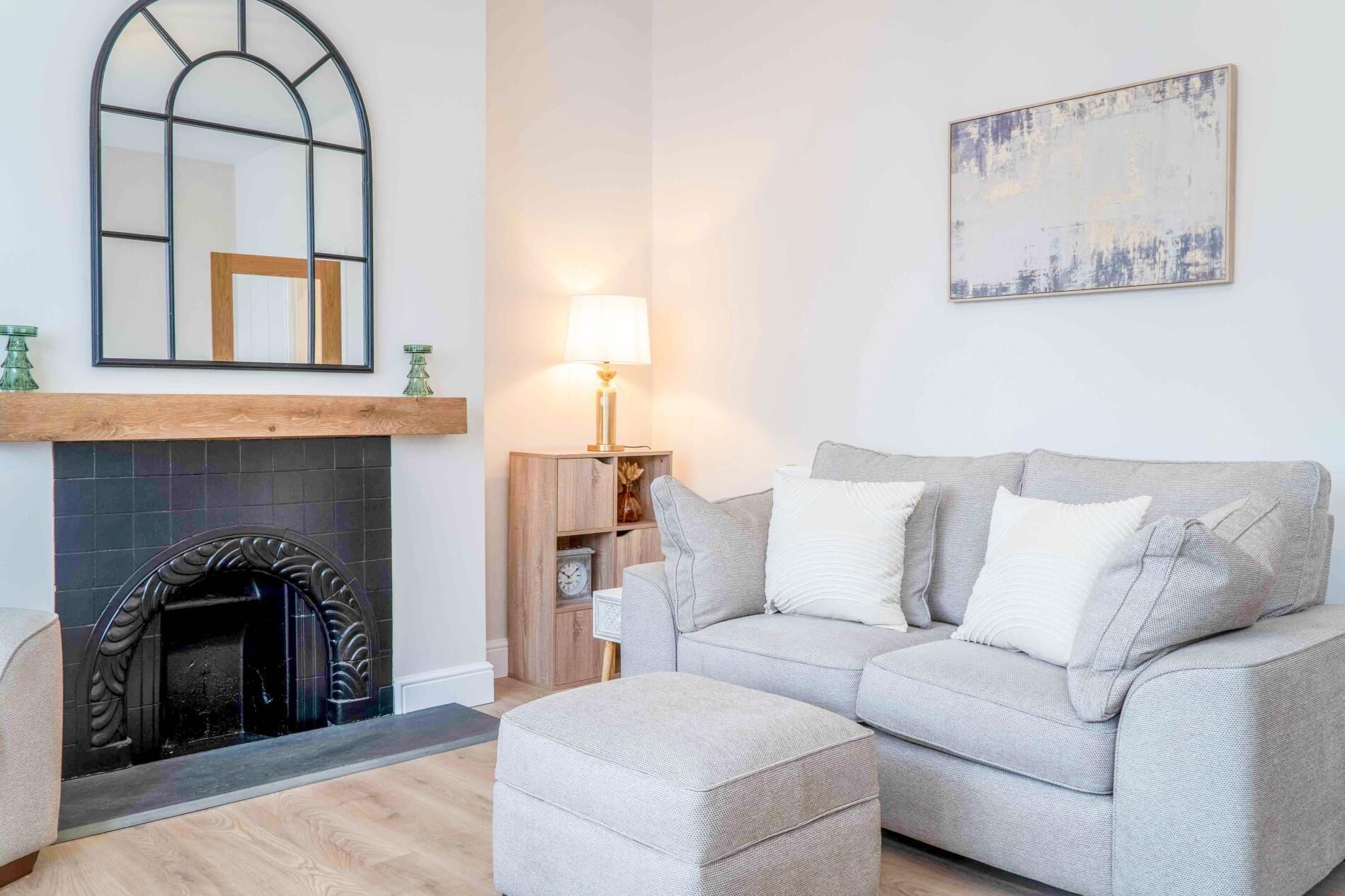 Un salon avec une cheminée, un canapé, un pouf, une lampe et un tableau au mur.