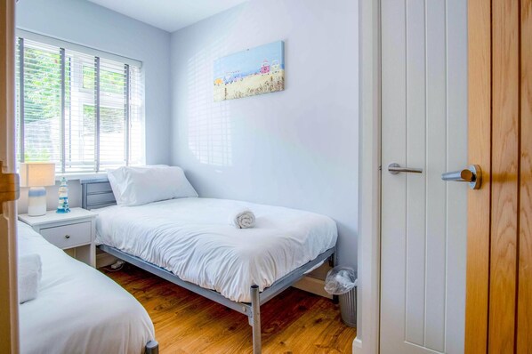 A bedroom with a single bed, a nightstand, a lamp, and a window with blinds.