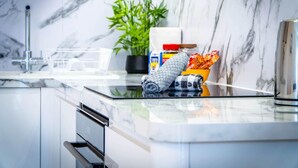A modern kitchen with a marble backsplash, a glass countertop, a bamboo plant, and a bowl of snacks. - Station Road - 1 Bedroom Apt - Burry Port (Burry Port)