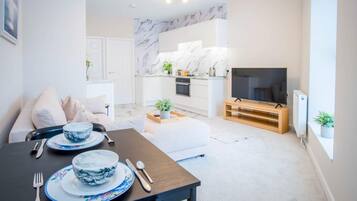 A modern living room with a dining area, a kitchen with marble backsplash, and a flat-screen TV.