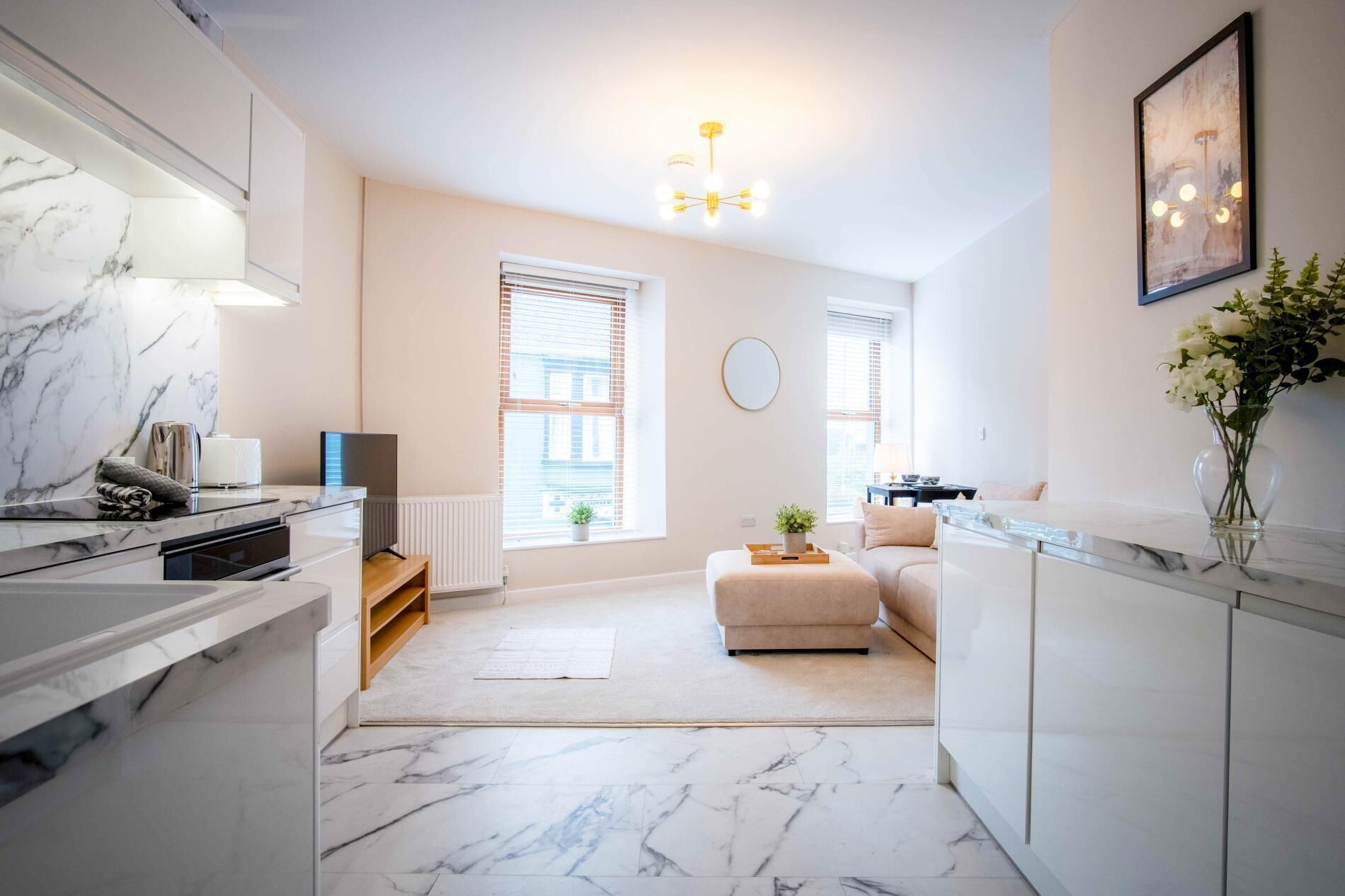 A modern kitchen with marble countertops, a built-in oven, and a dining area with a sofa and a small table.