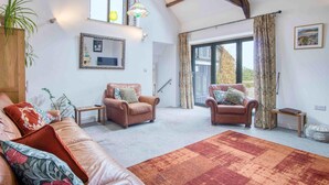 A spacious living room with two leather sofas, a large rug, and a wooden cabinet. - West Barn - 2 Bedroom Cottage - Llandeilo (Llandeilo)