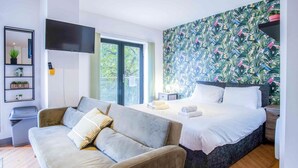 A modern bedroom with a sofa, a bed, a TV, and a tropical wallpaper.
