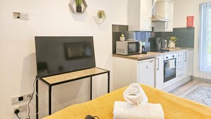Una moderna camera d'hotel con un letto, una televisione a schermo piatto, un piccolo tavolo, un forno a microonde, un bollitore e un lavello nella zona cucina.