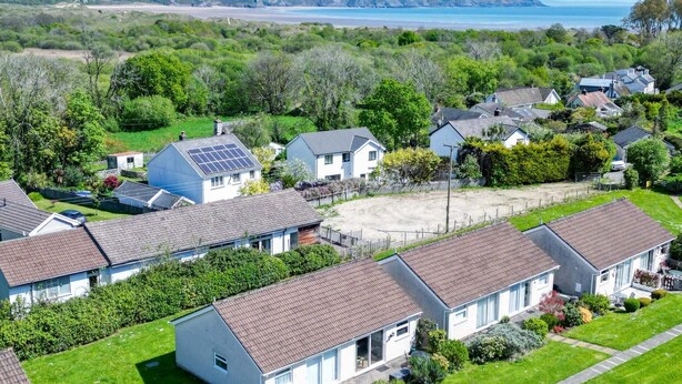 A residential area with houses featuring pitched roofs, some with solar panels, surrounded by greenery and a beach in the background. - Bayview 72 - 2 Bedroom Chalet - Bayview Oxwich (Swansea)