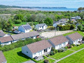 Zona residencial con casas de techo inclinado, algunas con paneles solares, rodeada de vegetación y una playa al fondo.