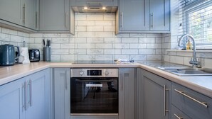A modern kitchen with grey cabinets, a built-in oven, and a stainless steel sink. - Bayview 72 - 2 Bedroom Chalet - Bayview Oxwich (Swansea)