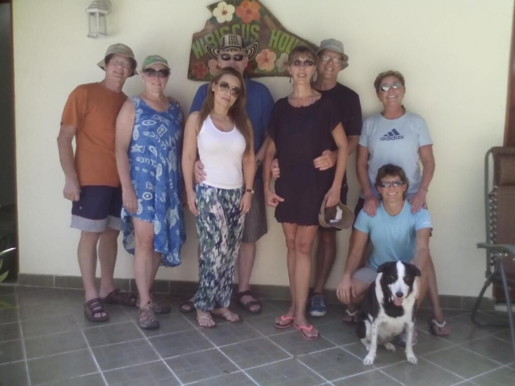 Un grupo de personas de pie en un espacio interior, un perro, un letrero con texto y una silla.