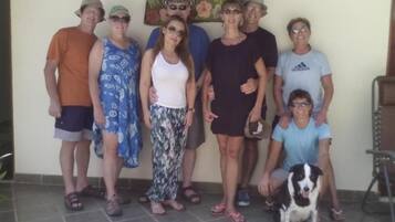 Un grupo de personas de pie en un espacio interior, un perro, un letrero con texto y una silla.