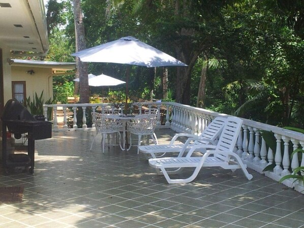An outdoor patio with white lounge chairs, a table, and umbrellas.