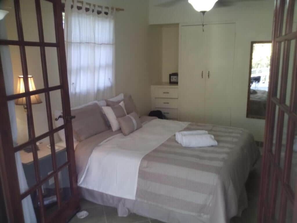 A bedroom with a bed, a nightstand, a lamp, a wardrobe, and a window with curtains.